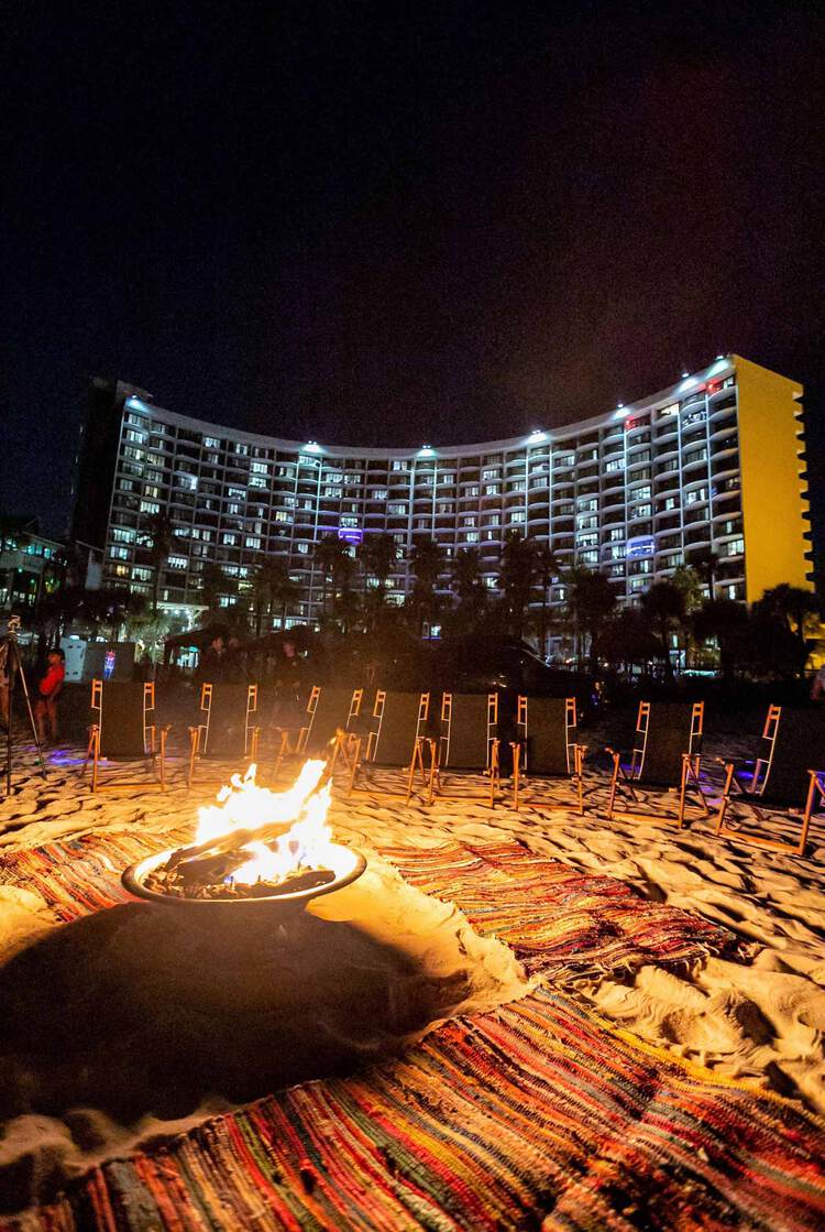 Fire pit on beach at night with view of illuminated resort in background