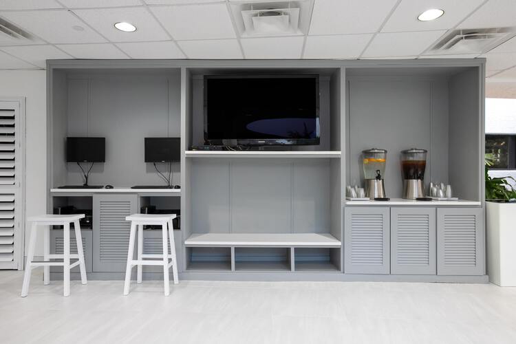 Gray wall unit with TV, monitors, seating area, and drink serving station