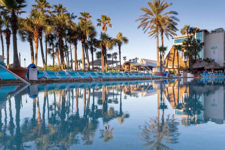 Pool area with blue lounge chairs, palm trees, and view of resort